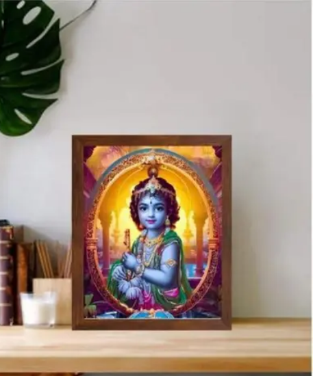 అందమైన ఫ్రేమ్డ్ బేబీ కృష్ణ వాల్ ఆర్ట్ – వైబ్రంట్ డిజిటల్ ప్రింట్, నెమలి ఈక కిరీటం, బంగారు ఆభరణాలు మరియు పూల దండతో శ్రీకృష్ణుడిని ప్రదర్శిస్తుంది, నిర్మలమైన నది మరియు ఆలయ నేపథ్యానికి ఎదురుగా సెట్ చేయబడింది – ఇల్లు, ఆలయం లేదా కార్యాలయ అలంకరణకు సరైనది. యొక్క చిత్రం